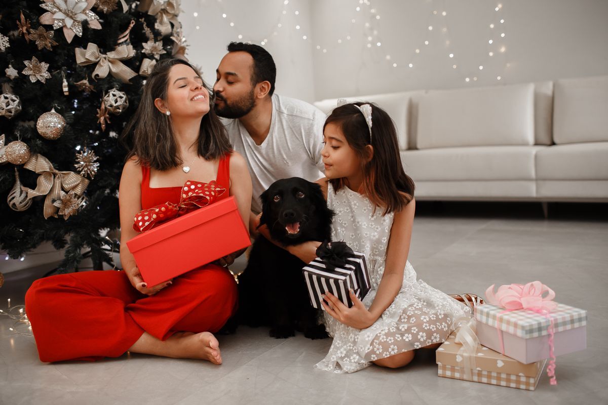 Familia con su perro negro junto al árbol de Navidad, intercambiando regalos