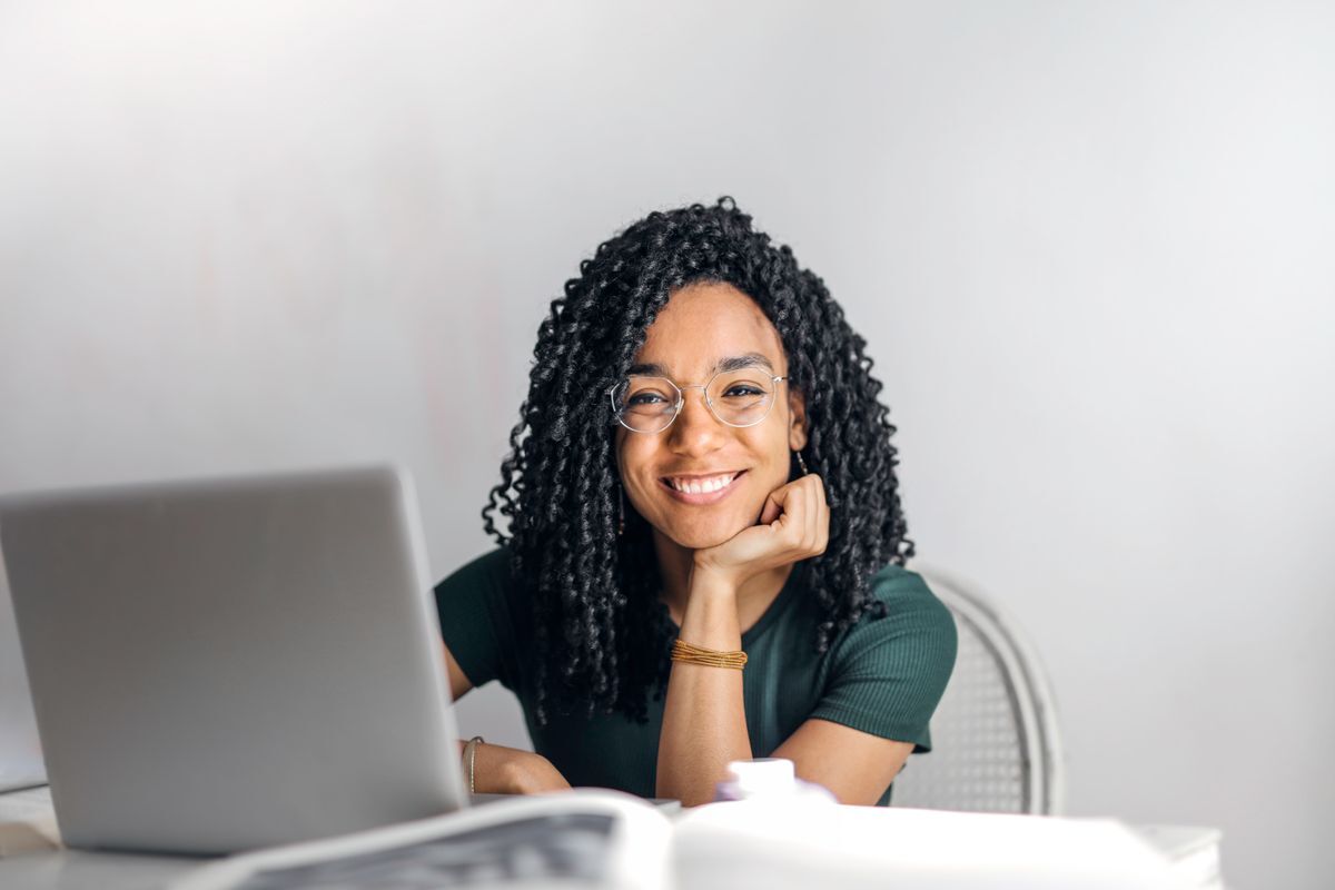 Mujer sonriendo frente a una computadora portátil, haciendo un trámite en línea desde casa